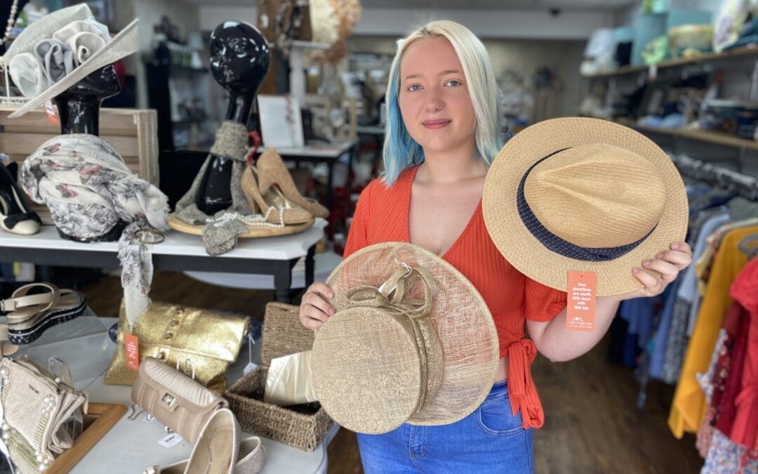 A photo of a girl smiling in a shop holding up two hats.