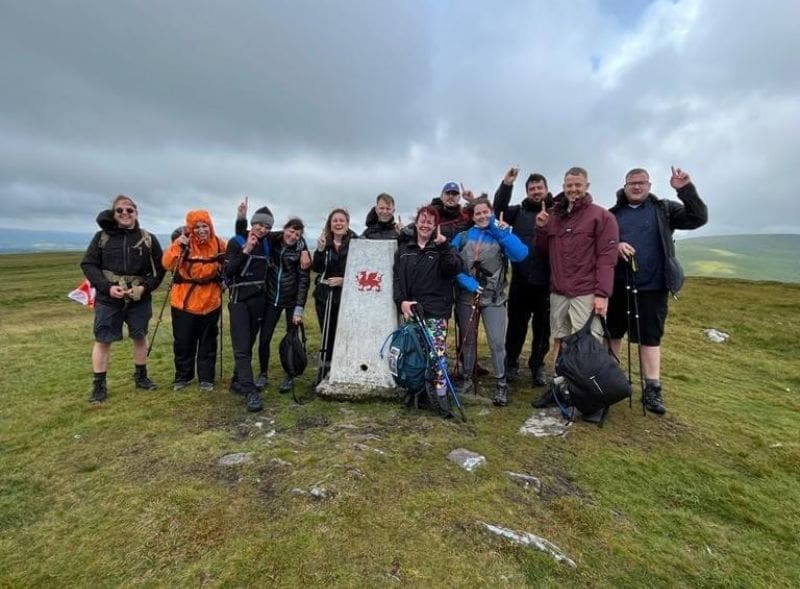 A group of trekkers posing with a stone monument in the Brecon Beacons.