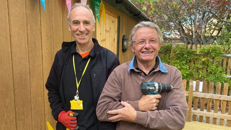 Stewart and Phil, Estates volunteers for Helen & Douglas House are standing in the Hospice garden. Phil is holding a drill.