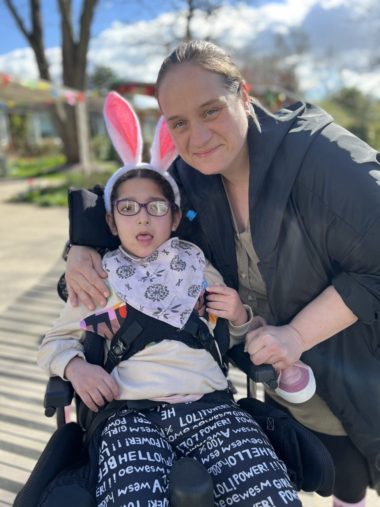 a little girl with bunny ears smiling in the hospice garden with her mum next to her