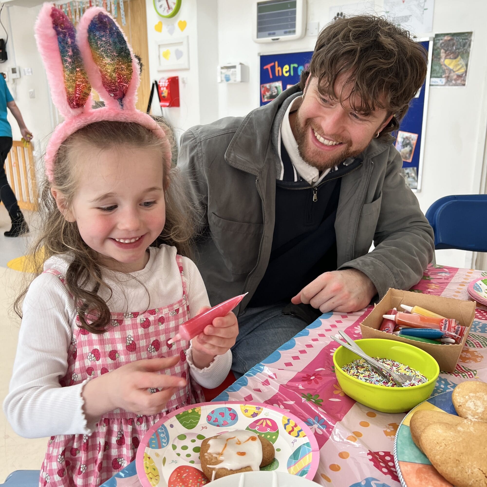 a little girl with bunny ears on smiling making easter biscuits with her father smiling at her