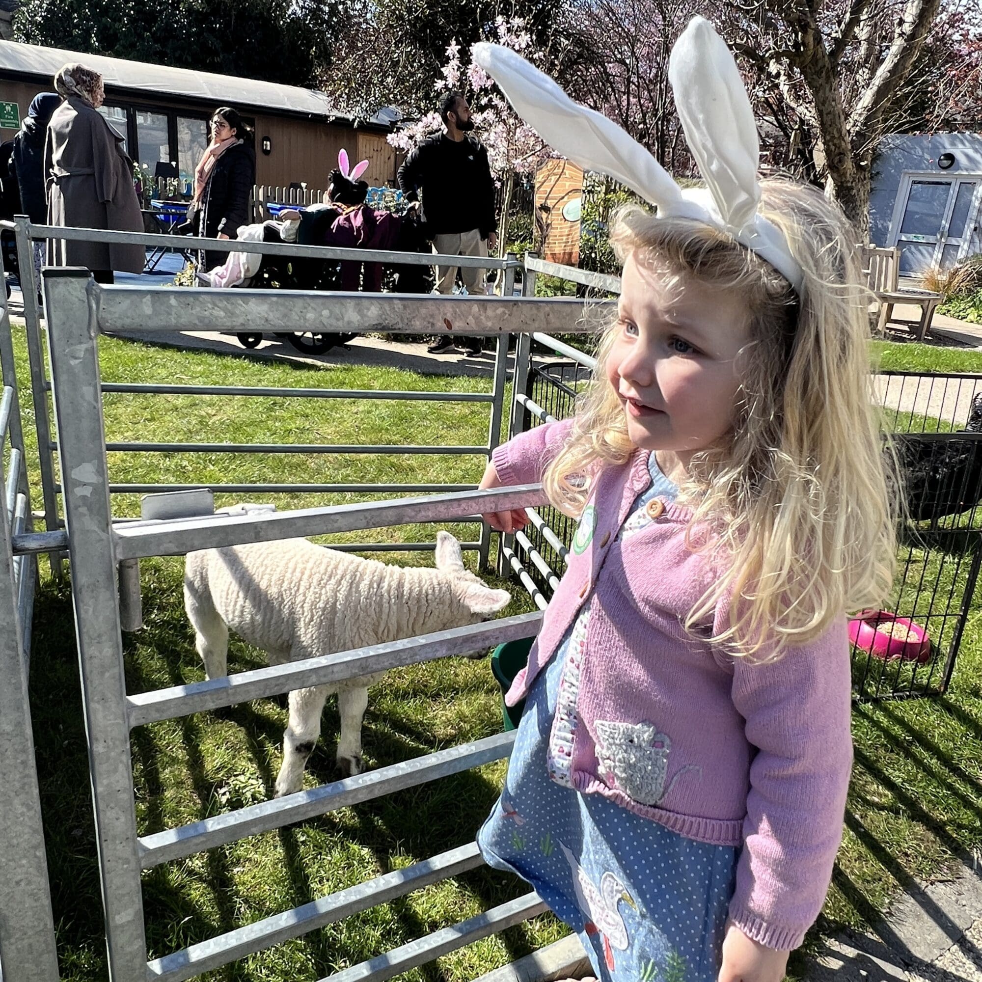 a little girl with bunny ears on smiling and pointing at a lamb