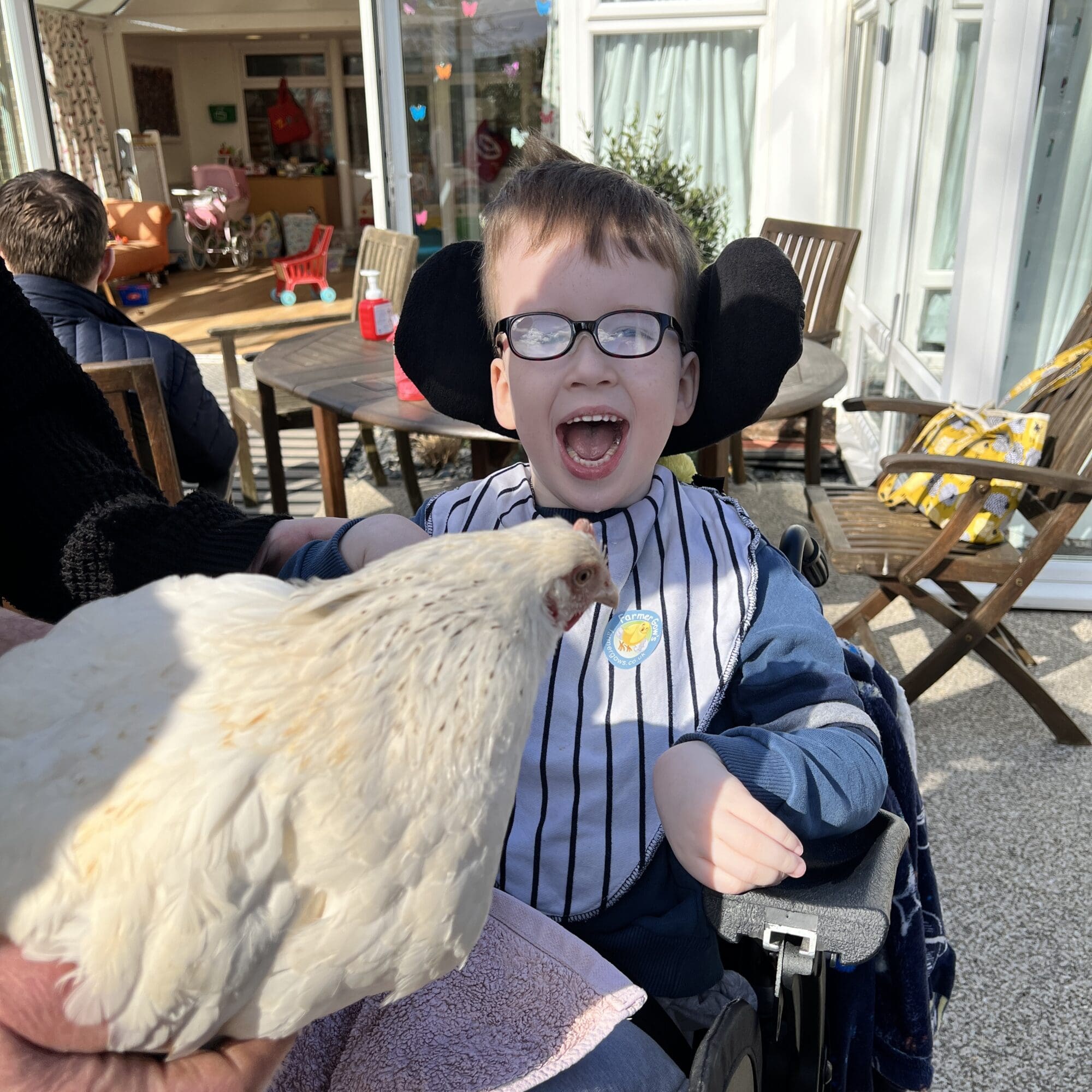 a boy smiling in a wheelchair with a chicken on his lap