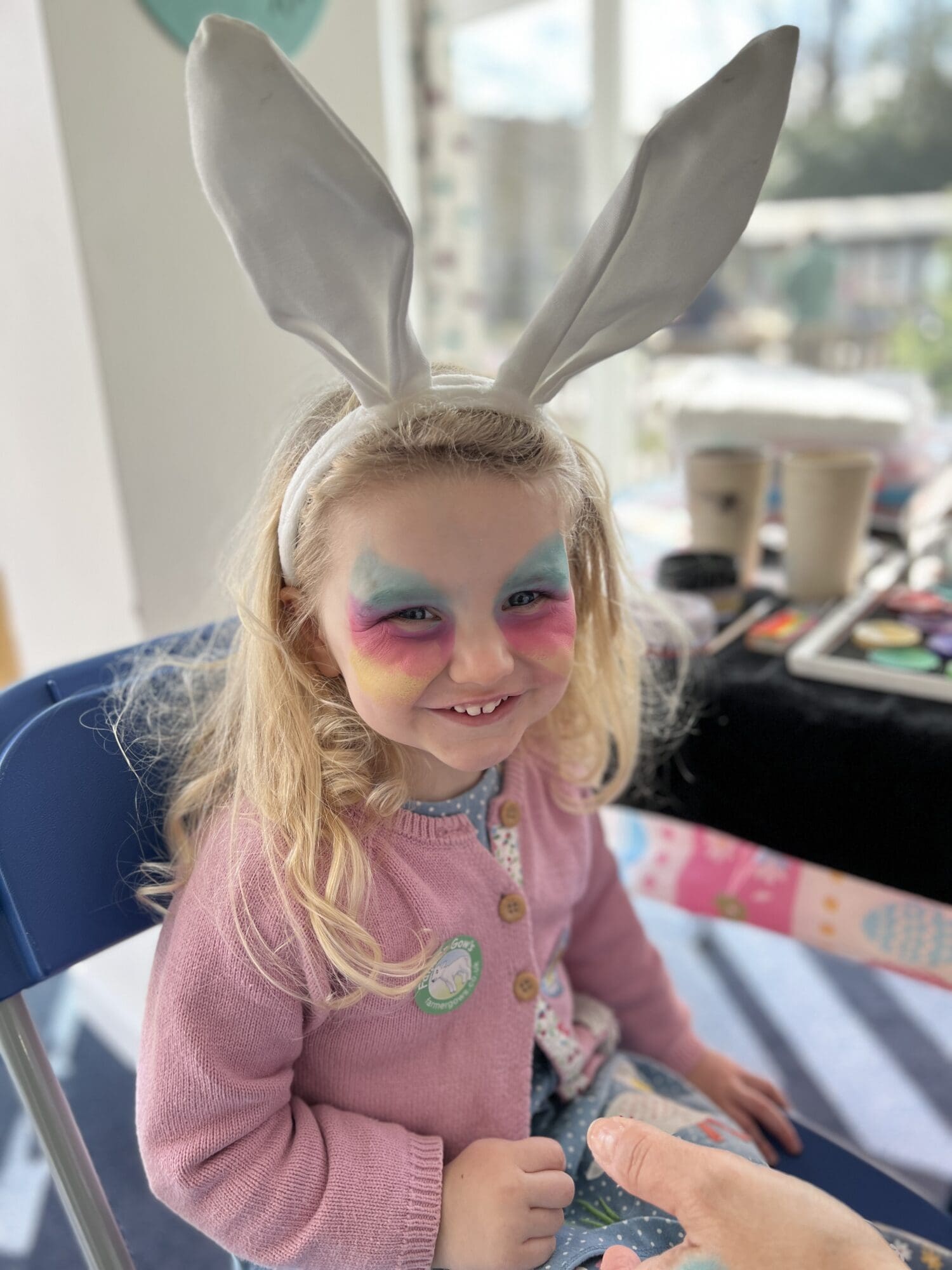 a blonde haired girl smiling with facepaint and a set of bunny ears on