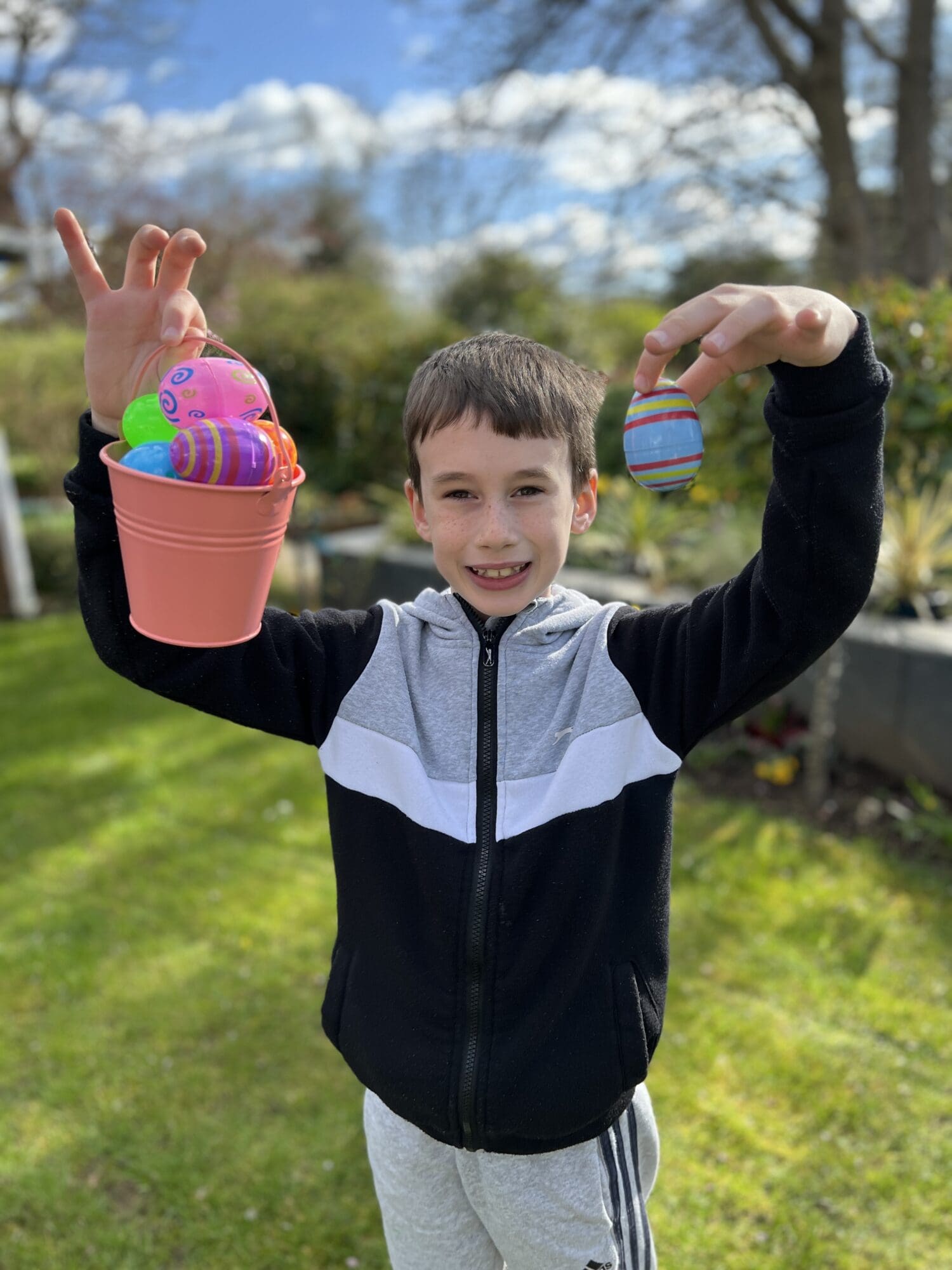 a boy smiling holding up a pink basket with easter eggs in it