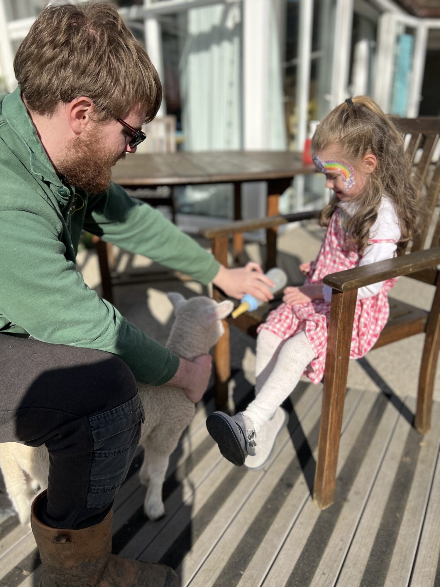 a little girl feeding a lamb sat down with a man in a green top