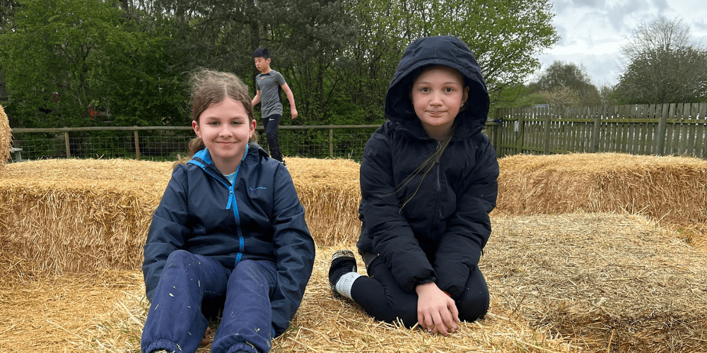 2 young girls sat on a hay bale